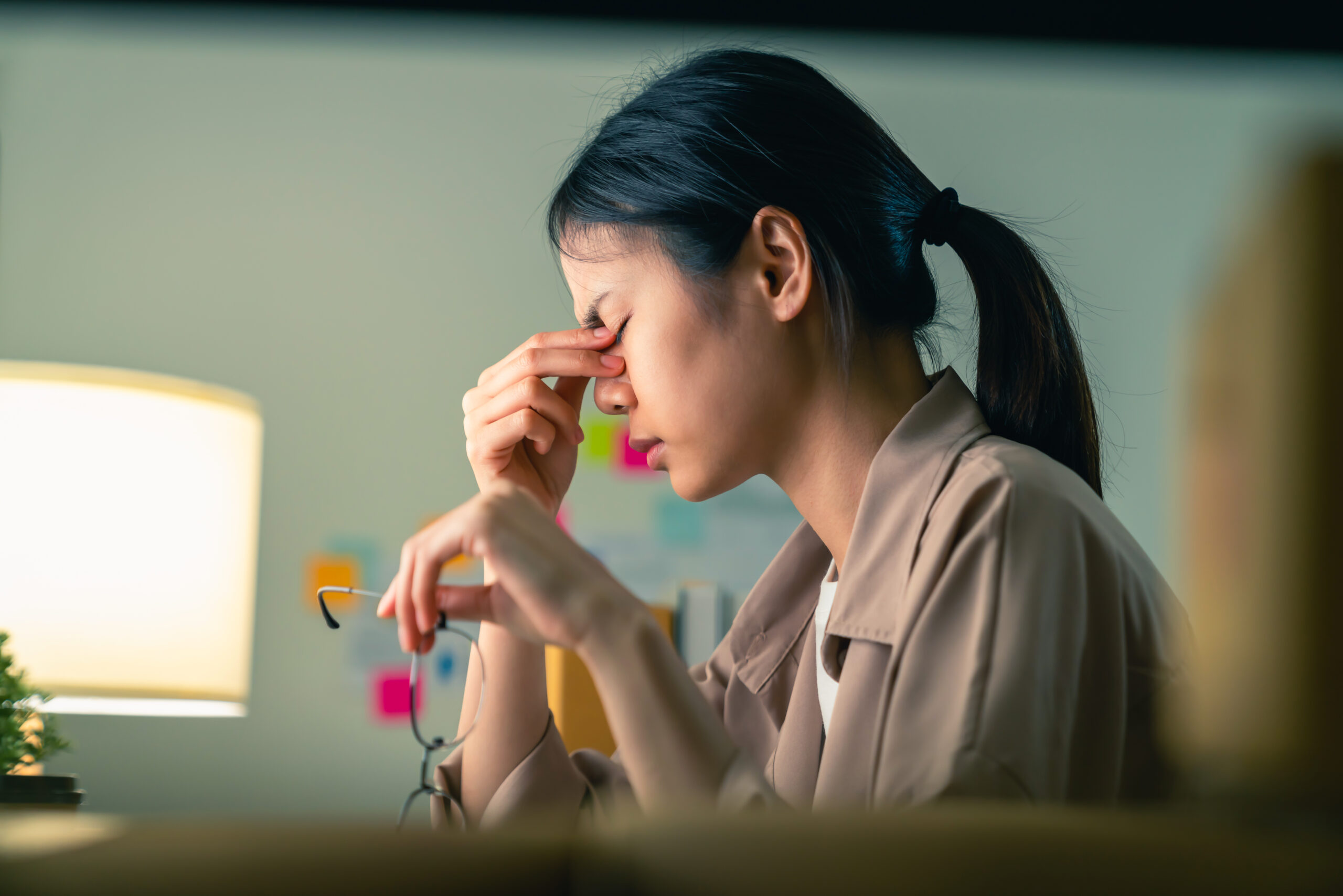 Young Asian woman sitting and holding glasses with hands touch the eyebrows have a headache because migraine.